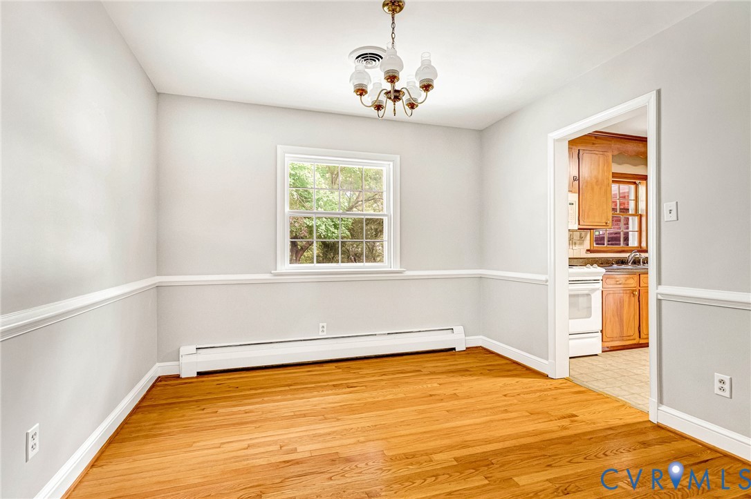 Hardwood flooring, chair rail molding, a window with exterior tree scenery, and a chandelier with glass shades