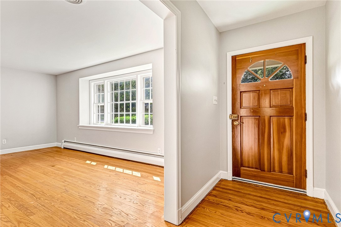 Warm wood-finish flooring throughout, bright paneled front door with an arched transom, and a multi-pane window with white trim Warm wood-finish flooring throughout, bright paneled front door with an arched transom, and a multi-pane window with white trim