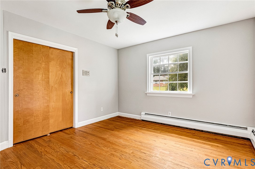 Hardwood flooring, light gray walls, white trim, window with grids, and a ceiling fan with light fixture