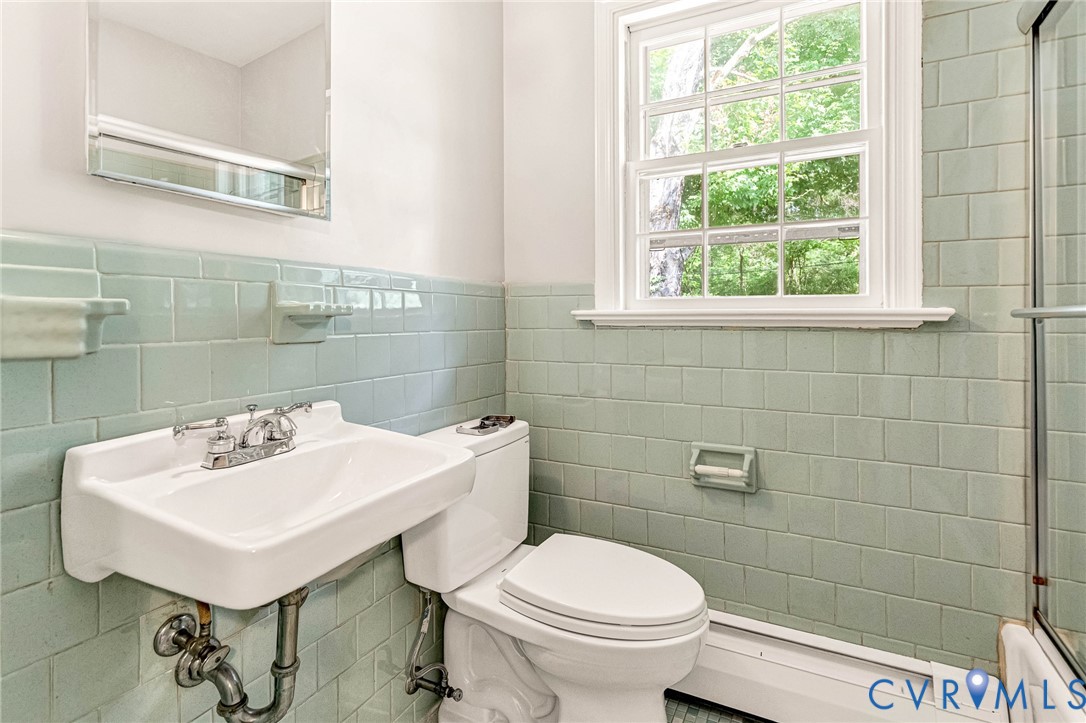 Wall-mounted vanity sink with chrome fixtures, complemented by subway tile wainscoting and a framed window