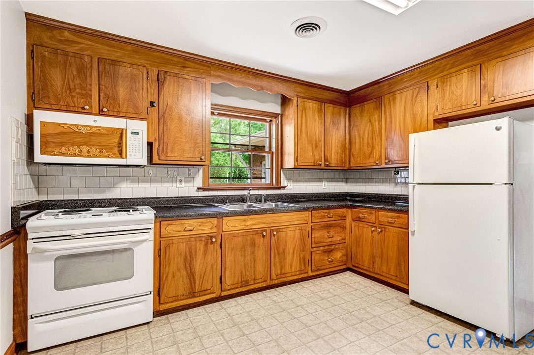 Wood cabinetry, dark countertops, white subway tile backsplash, and a window above the sink Wood cabinetry, dark countertops, white subway tile backsplash, and a window above the sink