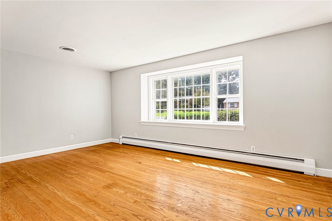 Hardwood flooring, light gray wall finish, white trim, and a window with muntins Hardwood flooring, light gray wall finish, white trim, and a window with muntins