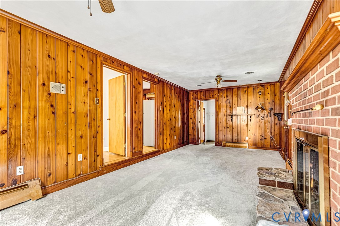 Brick fireplace with a stone hearth, wood-paneled walls, and light-colored carpet