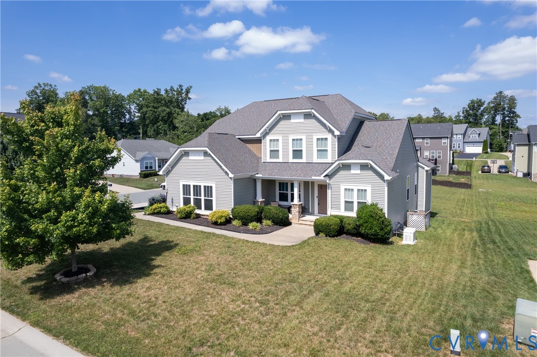 Craftsman-style home featuring light gray siding with white trim, a multi-pitch roof, and a neatly manicured lawn with established landscaping