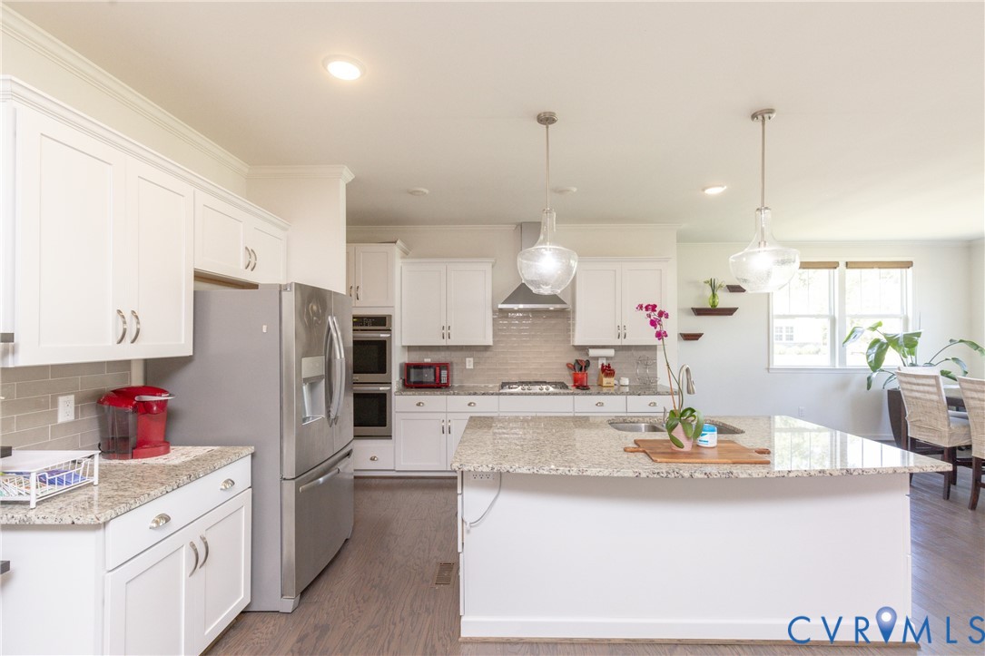 White cabinetry, stainless steel appliances, recessed lighting, wood-finish flooring, and a kitchen island with pendant lighting