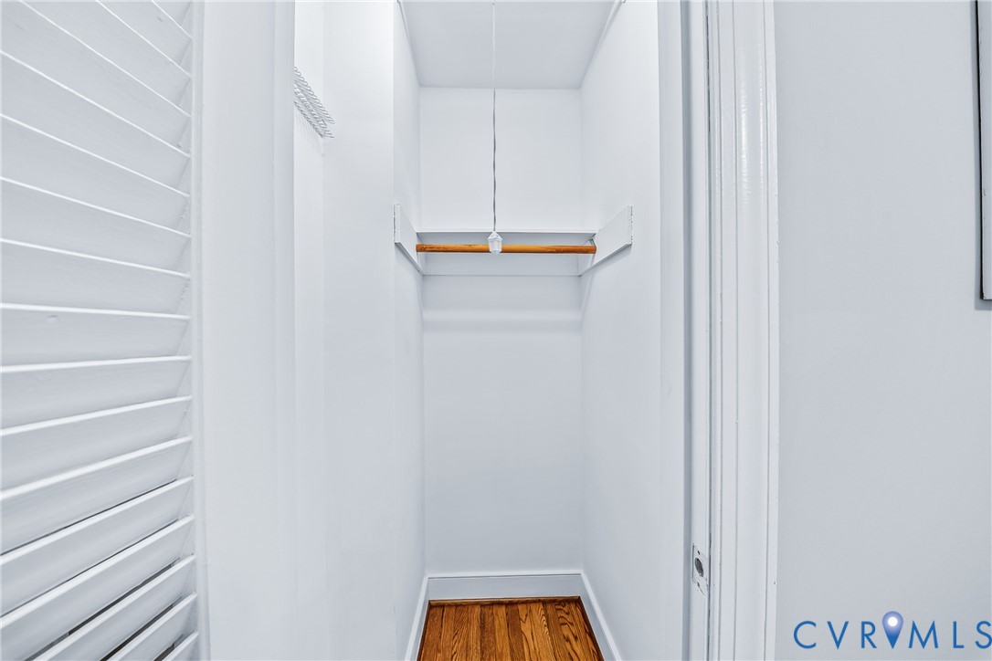 Closet with built-in wooden rod and shelf, hardwood flooring, and louvered door