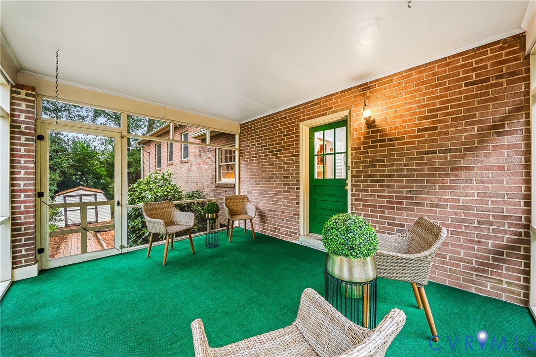 Screened porch featuring brick wall construction, green door with glass paneling, and an outdoor light fixture