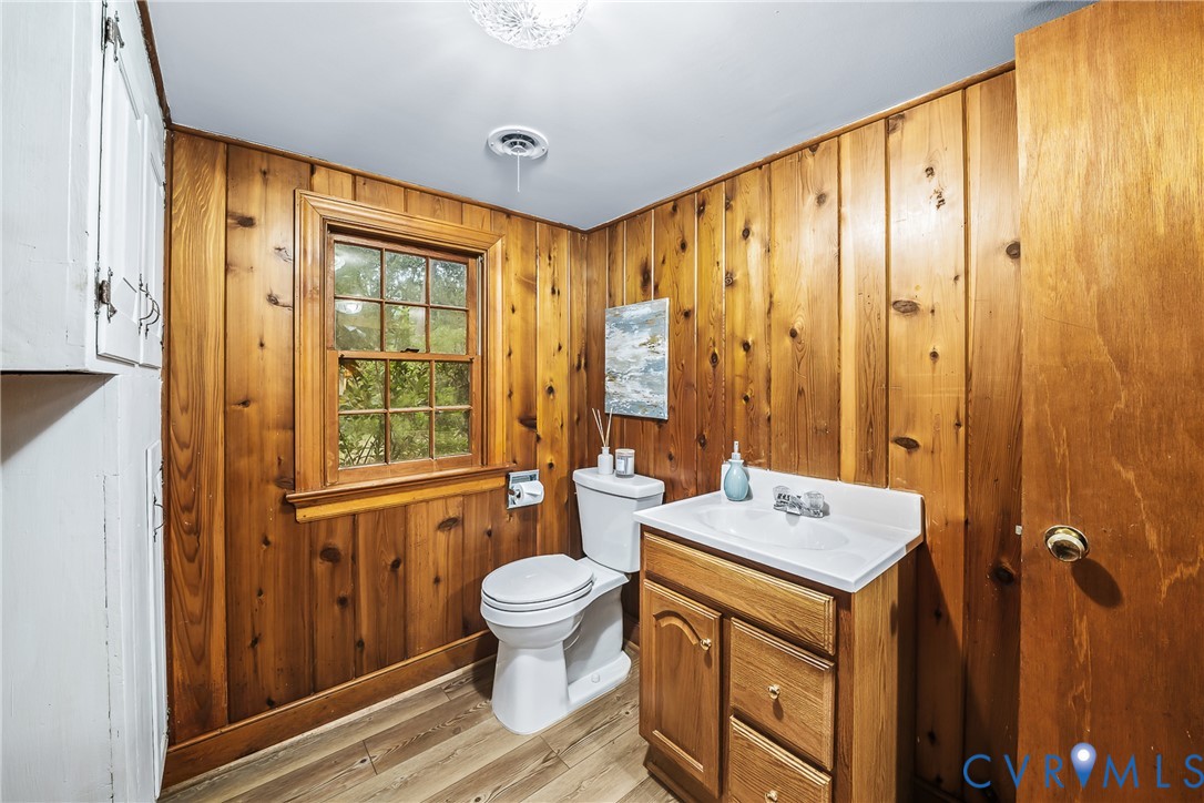 Wood paneling throughout, white ceiling with flush-mount lighting, wood-finish flooring, white vanity with integrated sink, and a window providing natural light