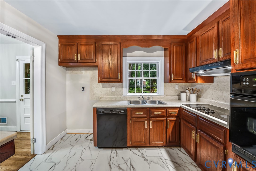 Kitchen featuring wood cabinetry, stainless steel double basin sink, electric cooktop, built-in oven, and white marble-look tile flooring Kitchen featuring wood cabinetry, stainless steel double basin sink, electric cooktop, built-in oven, and white marble-look tile flooring