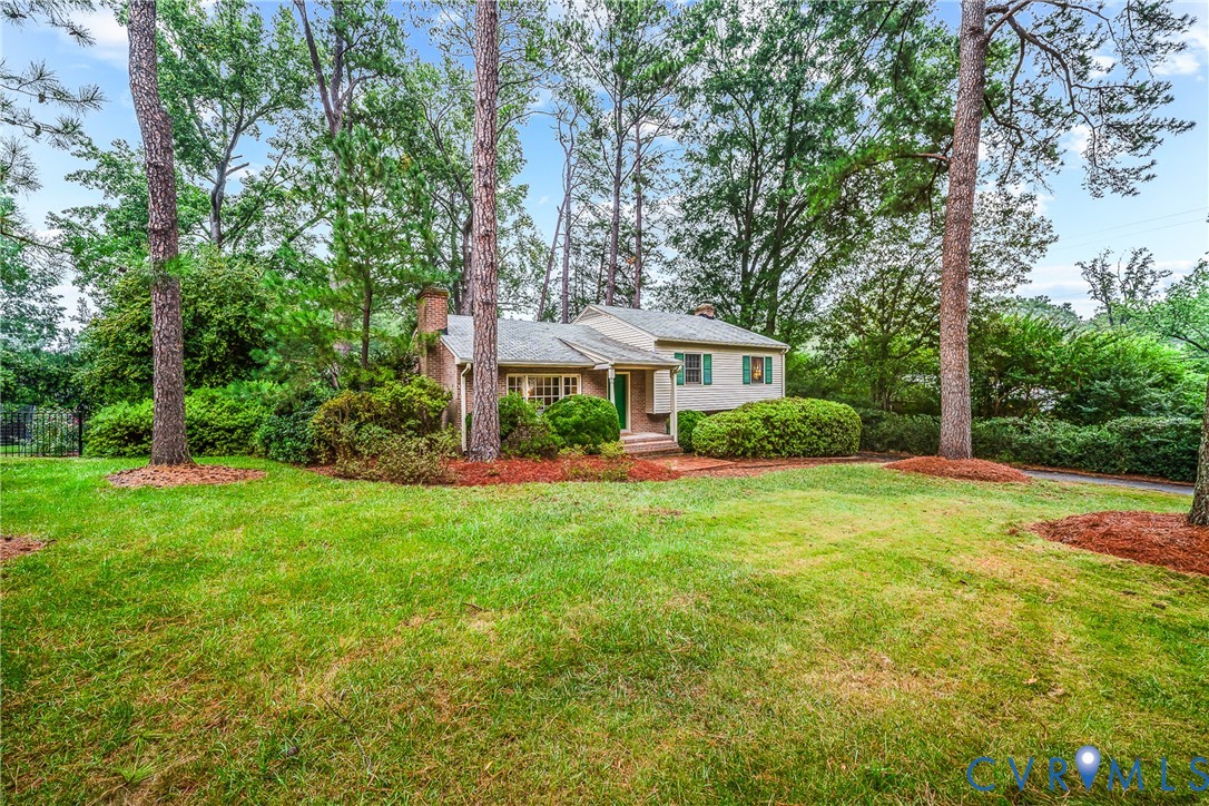 Brick exterior residence with a partial white facade, green window shutters, a front porch with a green door, and mature trees Brick exterior residence with a partial white facade, green window shutters, a front porch with a green door, and mature trees