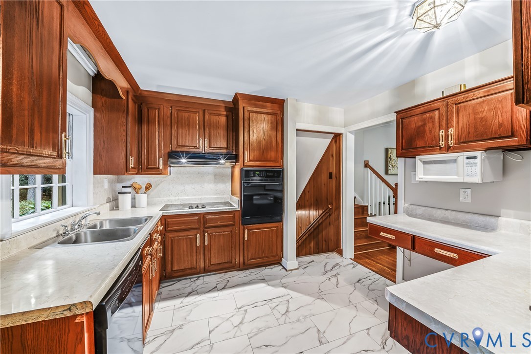 Kitchen featuring wood cabinetry, solid surface countertops, a stainless steel double basin sink, and integrated wall oven