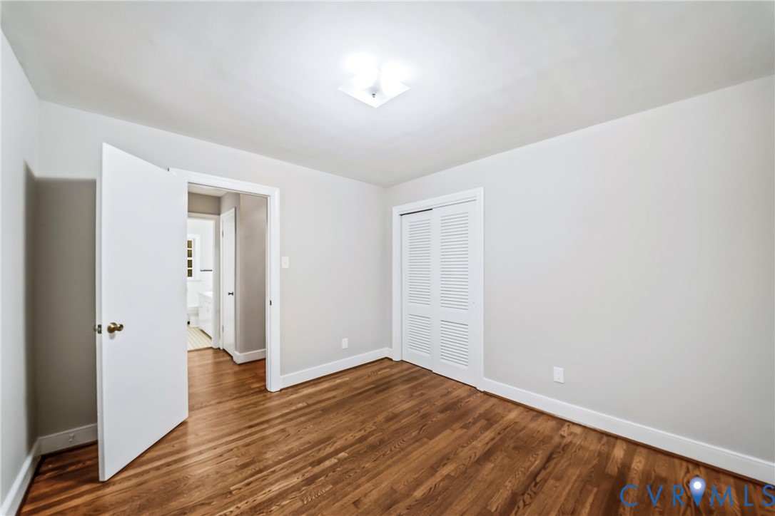 Wood-finish flooring, white walls, white trim, louvered bi-fold closet doors, and an overhead flush-mount light fixture