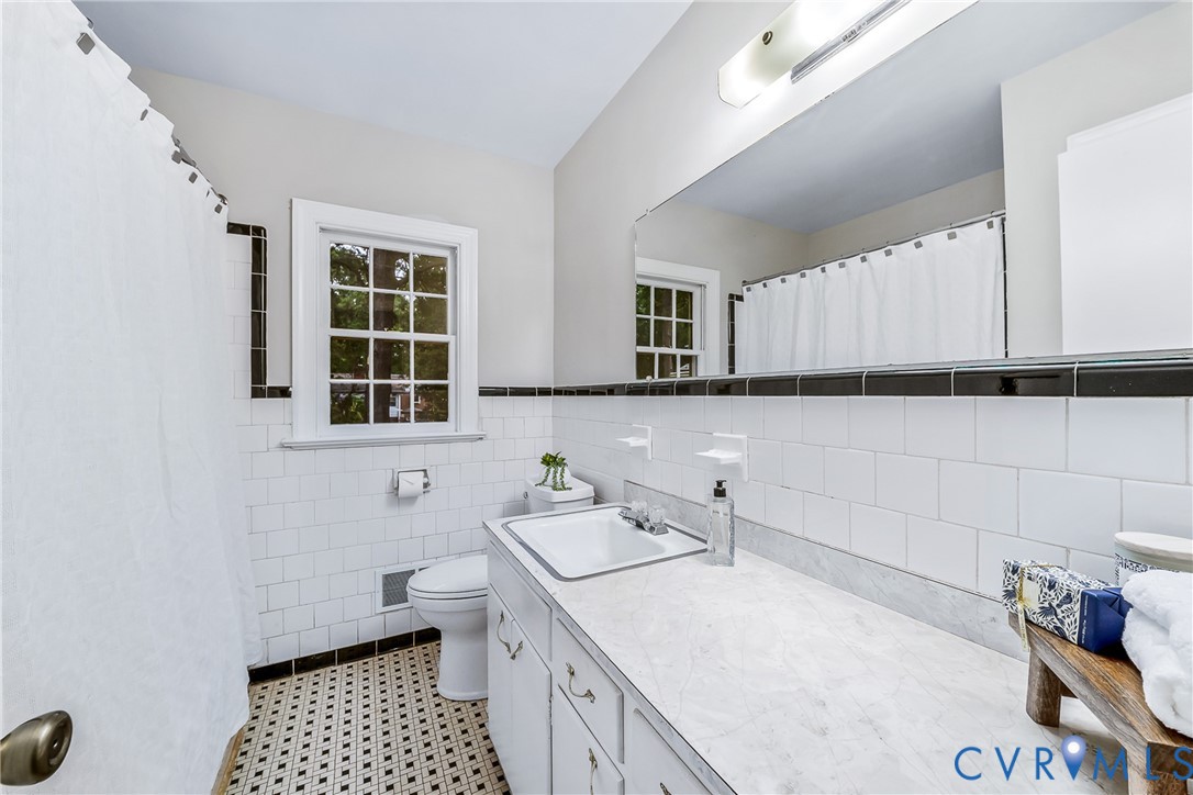 Bathroom featuring subway tile walls with black trim, a large vanity with an integrated sink, a window with muntins, and patterned floor tiles