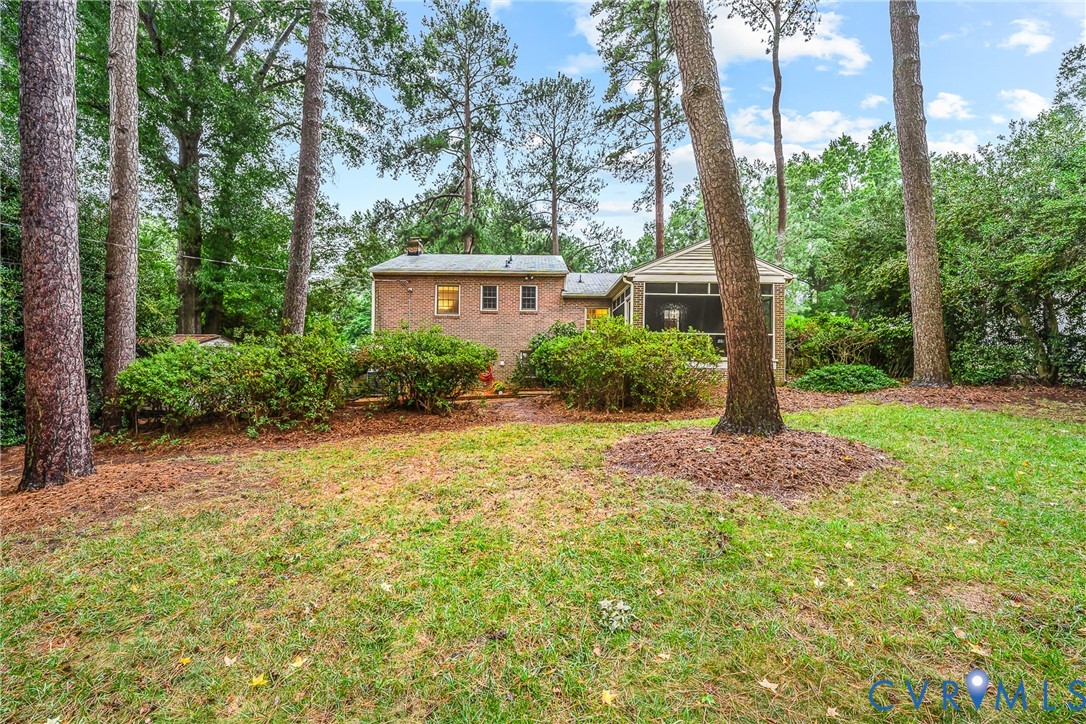 Expansive rear yard with mature trees, screened-in porch, and brick exterior