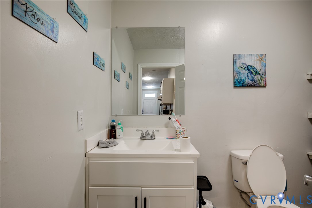 Bathroom featuring a white vanity with integrated sink, chrome faucet, wall-mounted mirror, and a white toilet