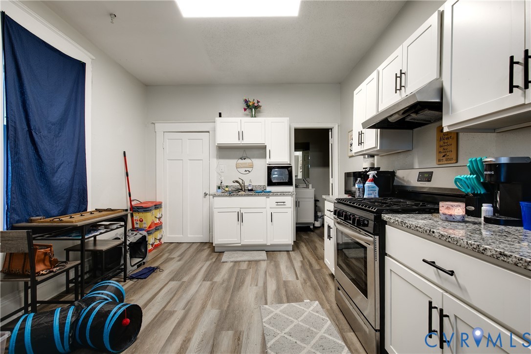 Contemporary kitchen featuring white cabinetry, black hardware, wood-finish flooring, stainless steel appliances, and light-colored countertops