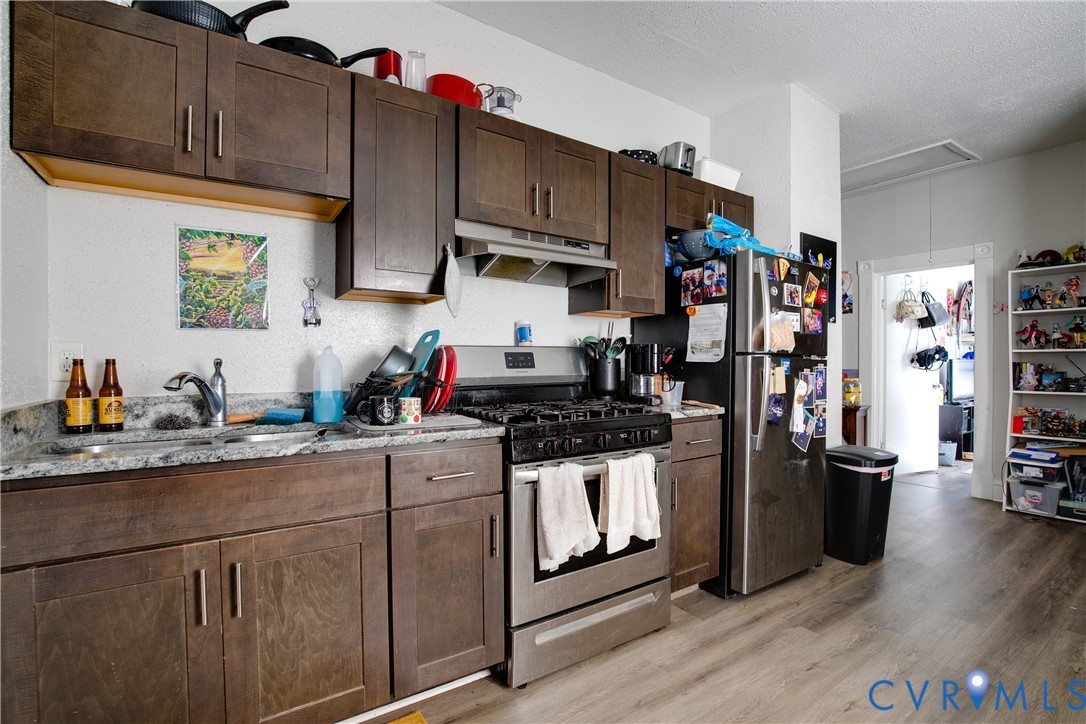 Galley kitchen featuring wood-finish flooring, dark wood-tone cabinetry with chrome hardware, a stainless steel gas range, and a stainless steel refrigerator