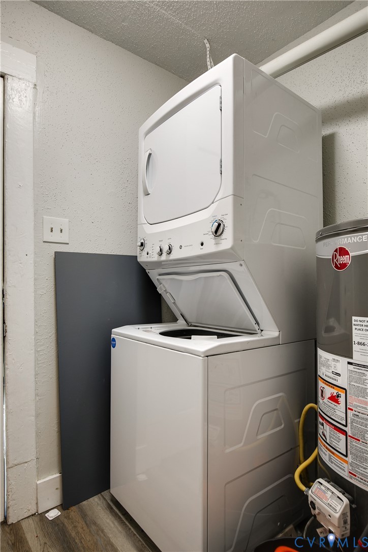 Stacked white washer and dryer unit, water heater, and wood-finish flooring