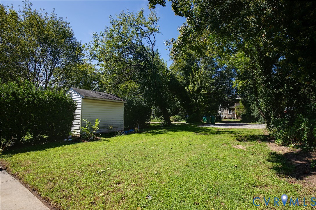 Detached storage shed with siding exterior, situated on a grassy lot with mature trees and established shrubbery
