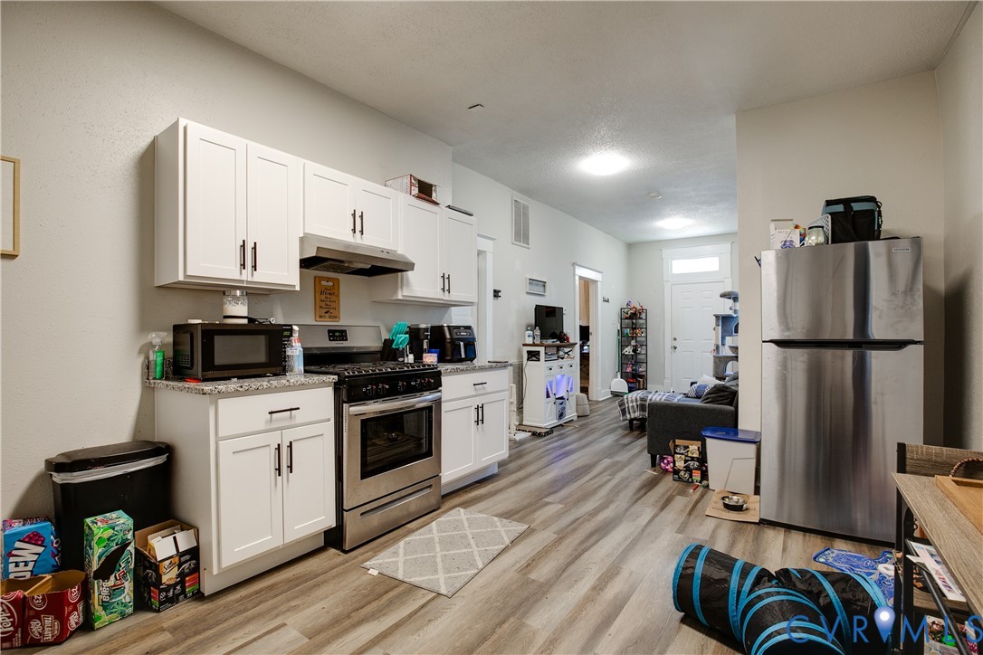 Kitchen featuring white shaker cabinetry, stainless steel appliances, granite-style countertops, and wood-finish flooring