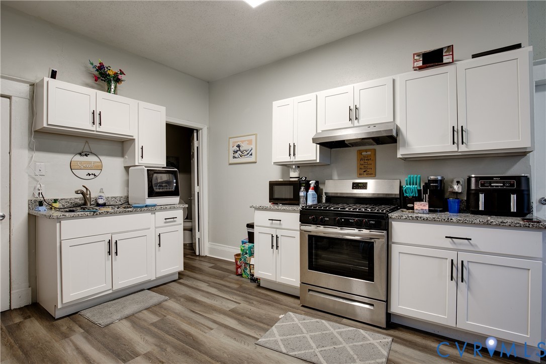 Kitchen featuring wood-finish flooring, white cabinetry with black hardware, stone-finish countertops, stainless steel appliances, and a stainless steel range hood