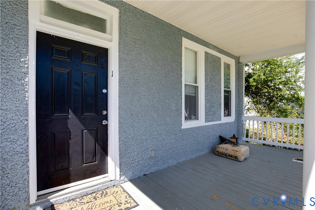 Covered porch with wood flooring, white railing, and paneled entry door with transom window