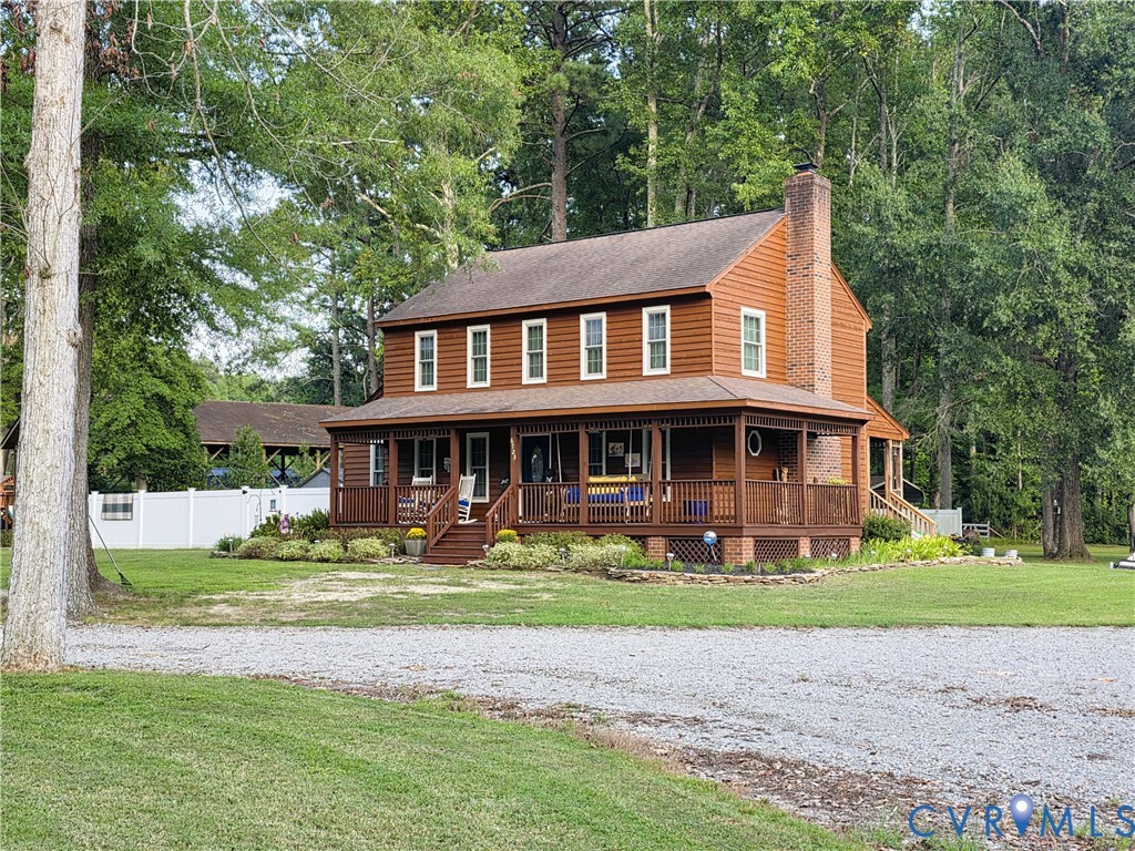 Two-story wood-sided exterior with a full-length covered porch, stone-accented chimney, and gravel driveway Two-story wood-sided exterior with a full-length covered porch, stone-accented chimney, and gravel driveway