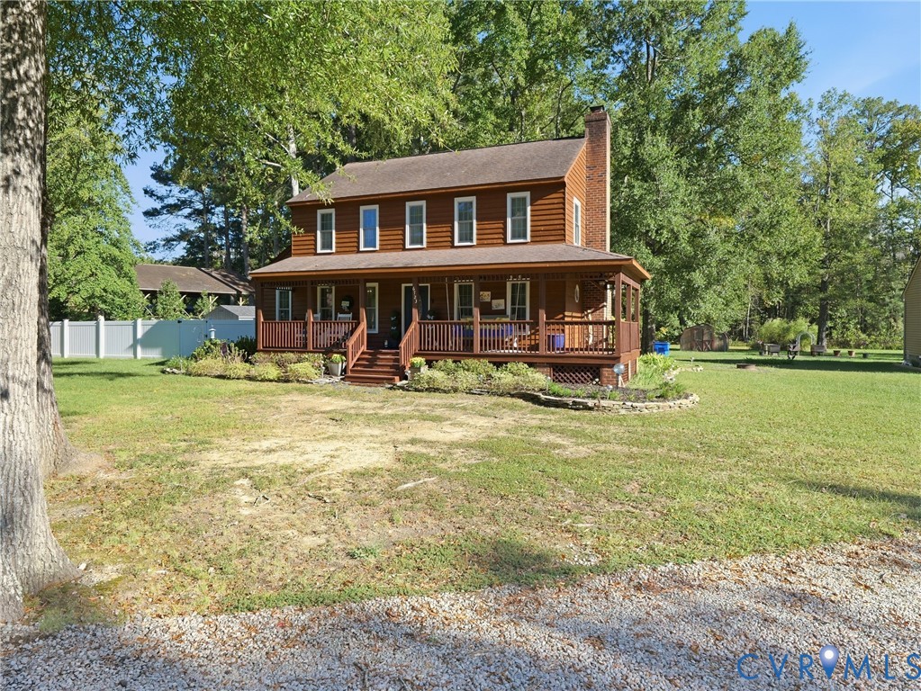 Two-story log cabin exterior featuring a wraparound covered porch, exterior brick chimney, stone-lined landscaping beds, and expansive yard Two-story log cabin exterior featuring a wraparound covered porch, exterior brick chimney, stone-lined landscaping beds, and expansive yard