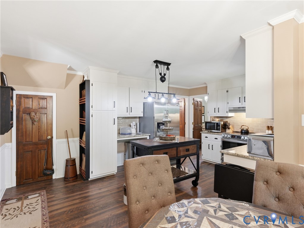 Kitchen featuring white cabinetry, wood-finish flooring, stone-style countertops, stainless steel appliances, and a hanging pulley-style light fixture