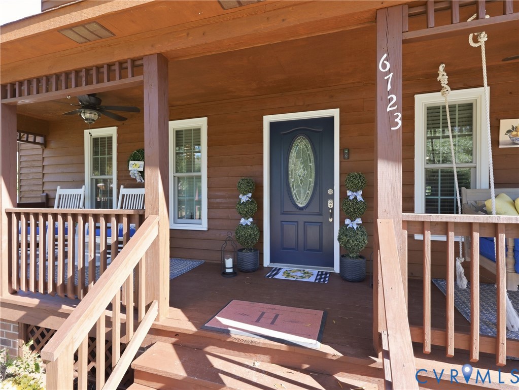 Covered wood-plank porch featuring a decorative lattice ceiling border, dark-finished entry door with an oval glass inset, and wood-finish railings