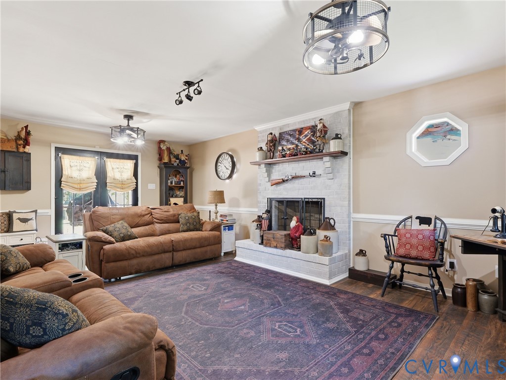 Light-toned brick fireplace with a wood mantel, dark wood-finish flooring, dual industrial-style cage ceiling light fixtures, and glass-paned double doors