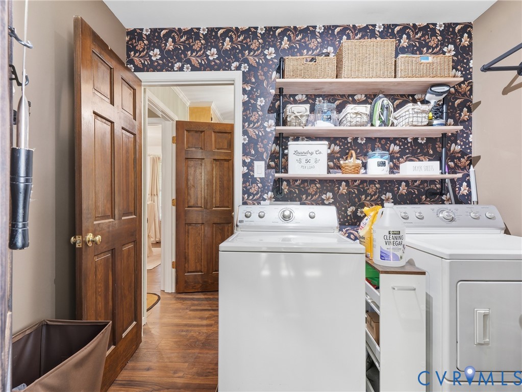 Laundry area featuring wood-finish flooring, decorative floral wall covering, and built-in industrial-style shelving with wood surfaces and black metal supports, complemented by solid wood doors