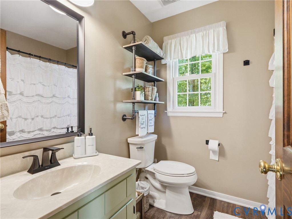 Vanity with an integrated sink and light-toned solid surface countertop, matte black faucet, framed mirror, industrial-style pipe shelving, and wood-finish flooring