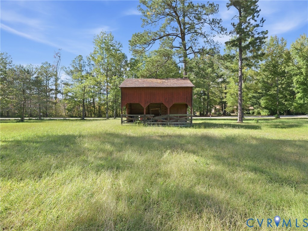 Open acreage featuring a rustic wood-sided outbuilding with an attached rail fence and mature perimeter trees