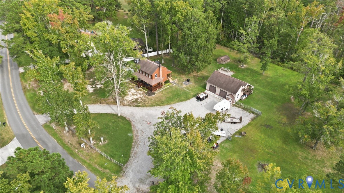 Wooded lot with a gravel driveway, a two-story residence featuring a porch, and an additional garage structure