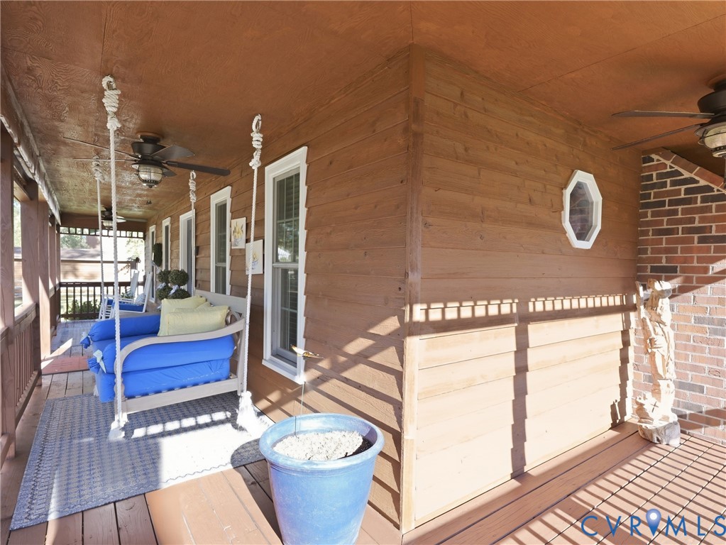 Covered porch featuring wood-plank siding, a red brick accent wall, white-trimmed windows, and ceiling-mounted fans