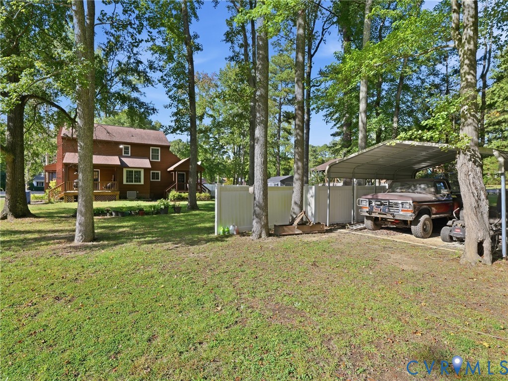 Expansive backyard featuring mature trees, white vinyl privacy fencing, and a metal-roofed carport Expansive backyard featuring mature trees, white vinyl privacy fencing, and a metal-roofed carport