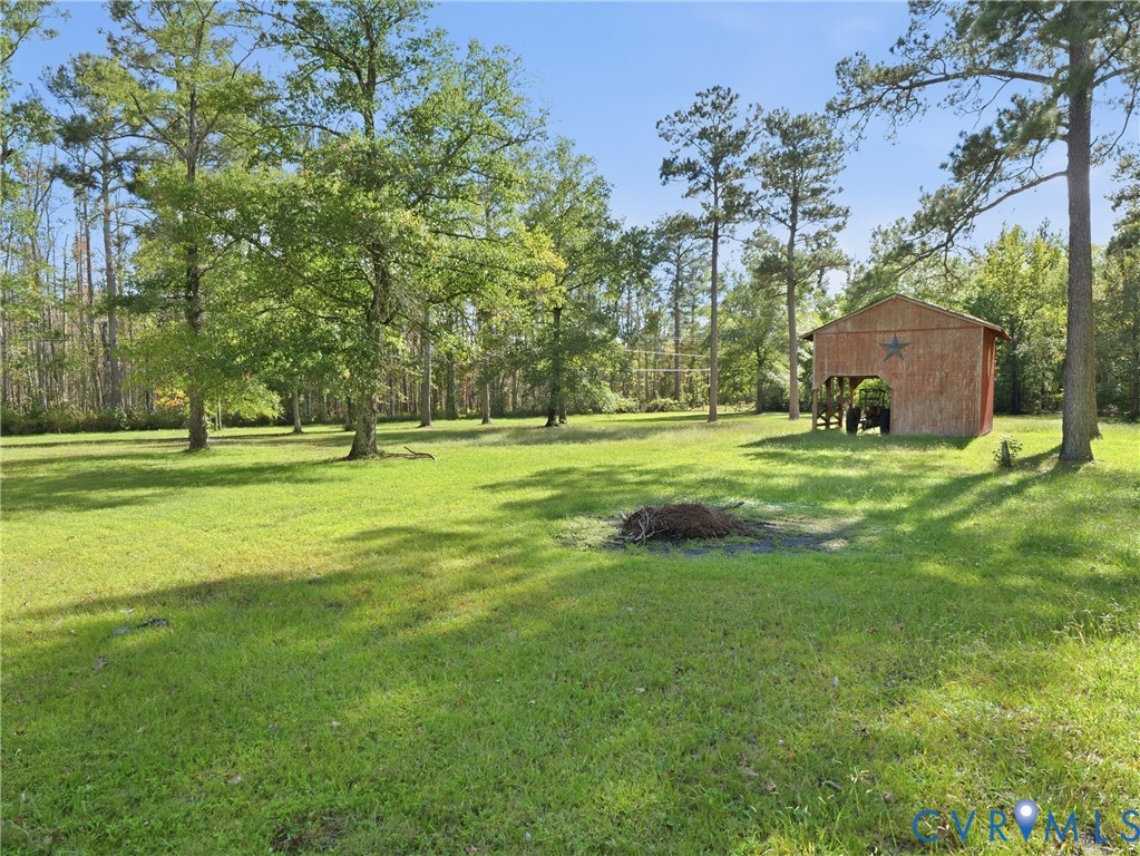 Expansive grounds featuring mature shade trees, open grassy areas, and a detached wood-frame structure with an integrated covered storage bay