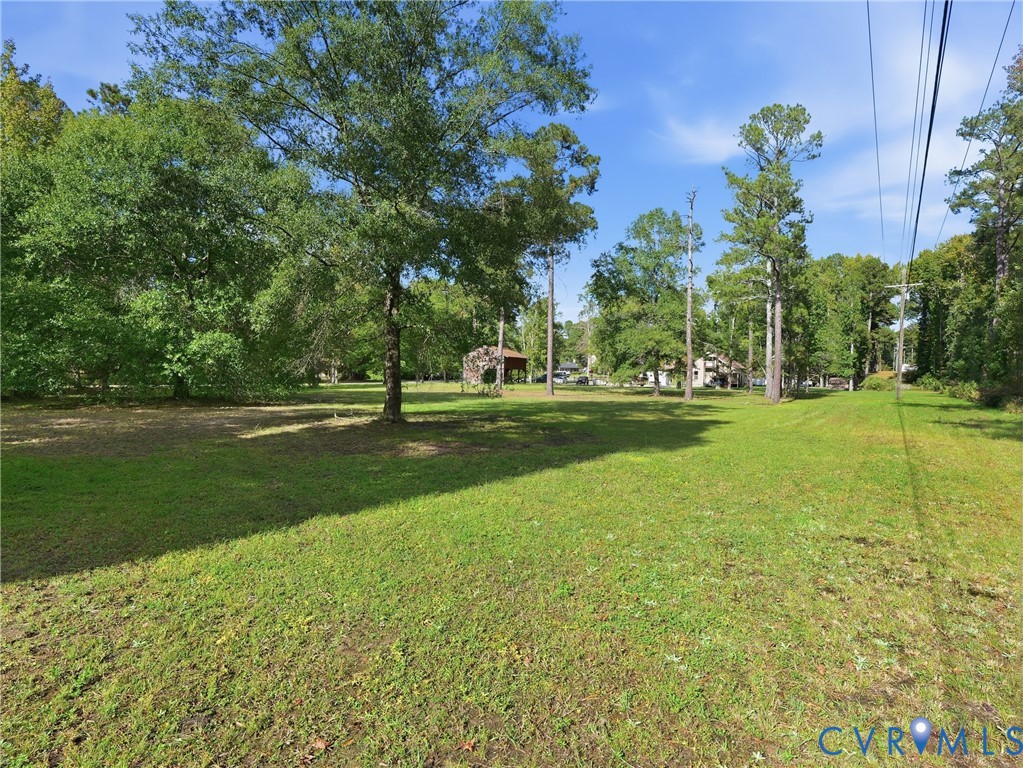 Expansive lot featuring mature trees, open grassy terrain, and an existing detached covered structure