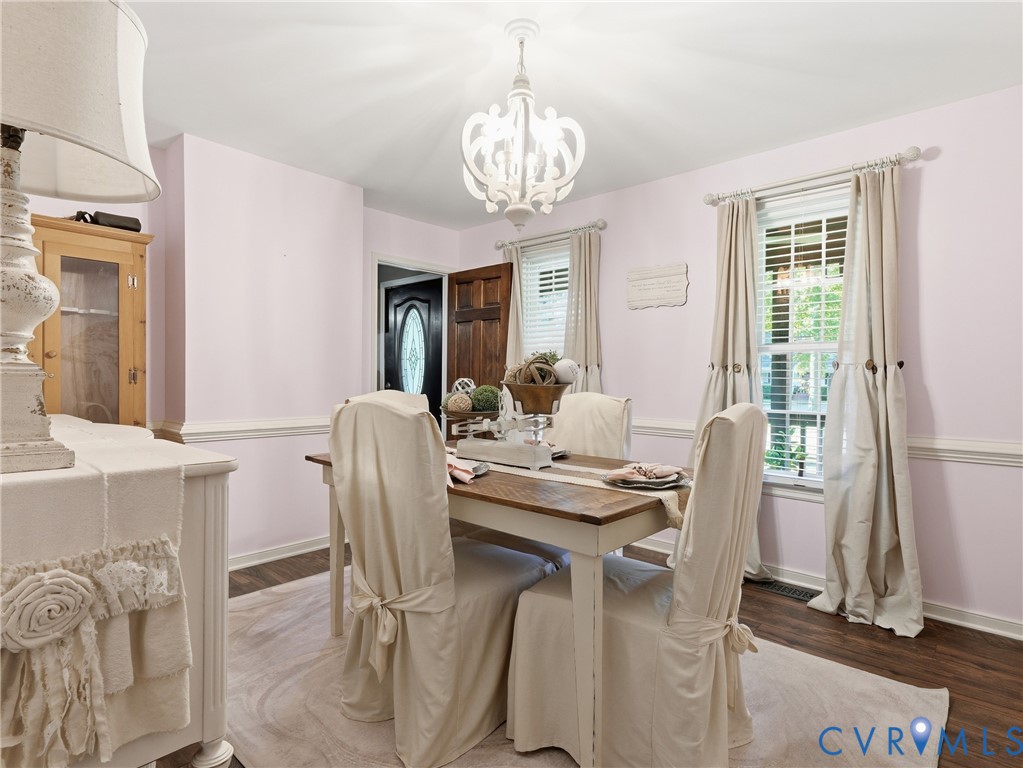 Dining space featuring wood-finish flooring, decorative chair rail molding, a white multi-arm chandelier, and a wood-paneled door with an oval glass insert