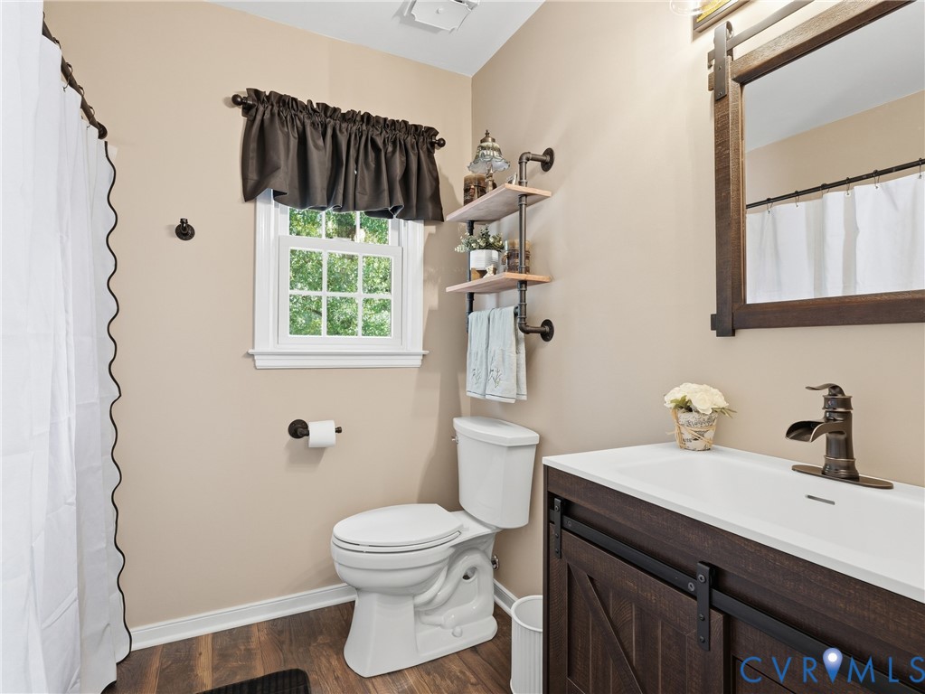 Bathroom featuring a wood-finish vanity with a white integrated sink, oil-rubbed bronze faucet, rustic wood-framed mirror, and wall-mounted industrial pipe shelving
