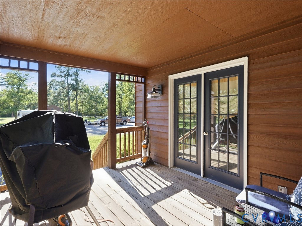 Covered porch featuring wood-finish siding, wood decking, glass-paneled double doors, and an attached exterior wall-mounted light fixture
