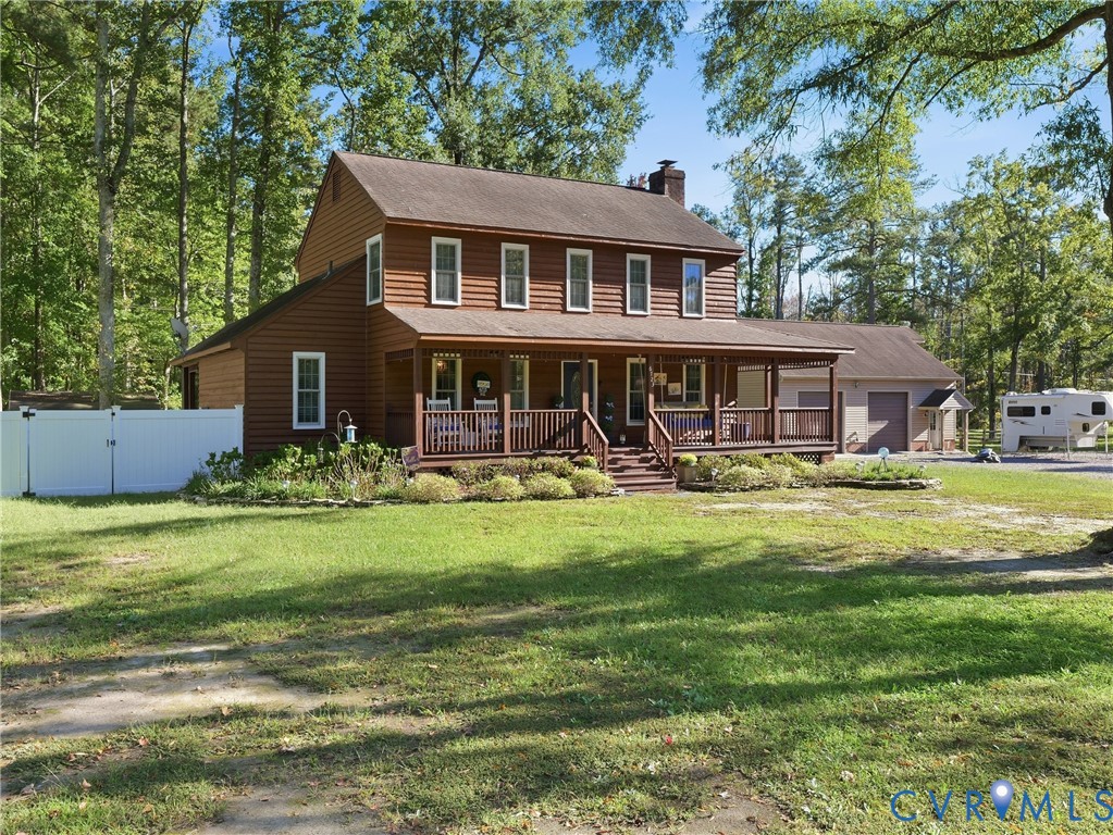 Two-story home with horizontal siding, a wrap-around porch featuring wood railing, a brick chimney, and a detached two-car garage, all situated on a wooded lot Two-story home with horizontal siding, a wrap-around porch featuring wood railing, a brick chimney, and a detached two-car garage, all situated on a wooded lot