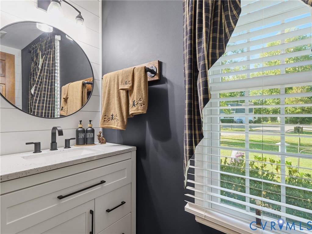 White vanity featuring a stone-composite countertop, undermount sink, and matte black hardware, accented by shiplap wall detailing, a circular mirror, and industrial-style metal pipe fixtures