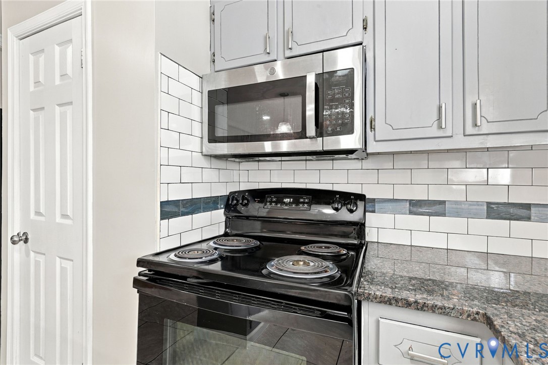 Kitchen featuring a black electric range, stainless steel microwave, light gray cabinetry, subway tile backsplash, and granite-style countertops