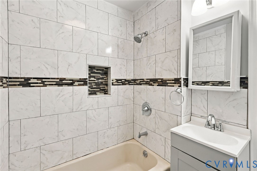 Bathtub with white subway tile surround, decorative mosaic tile accent band, built-in shower niche, and a chrome shower head with coordinating fixtures