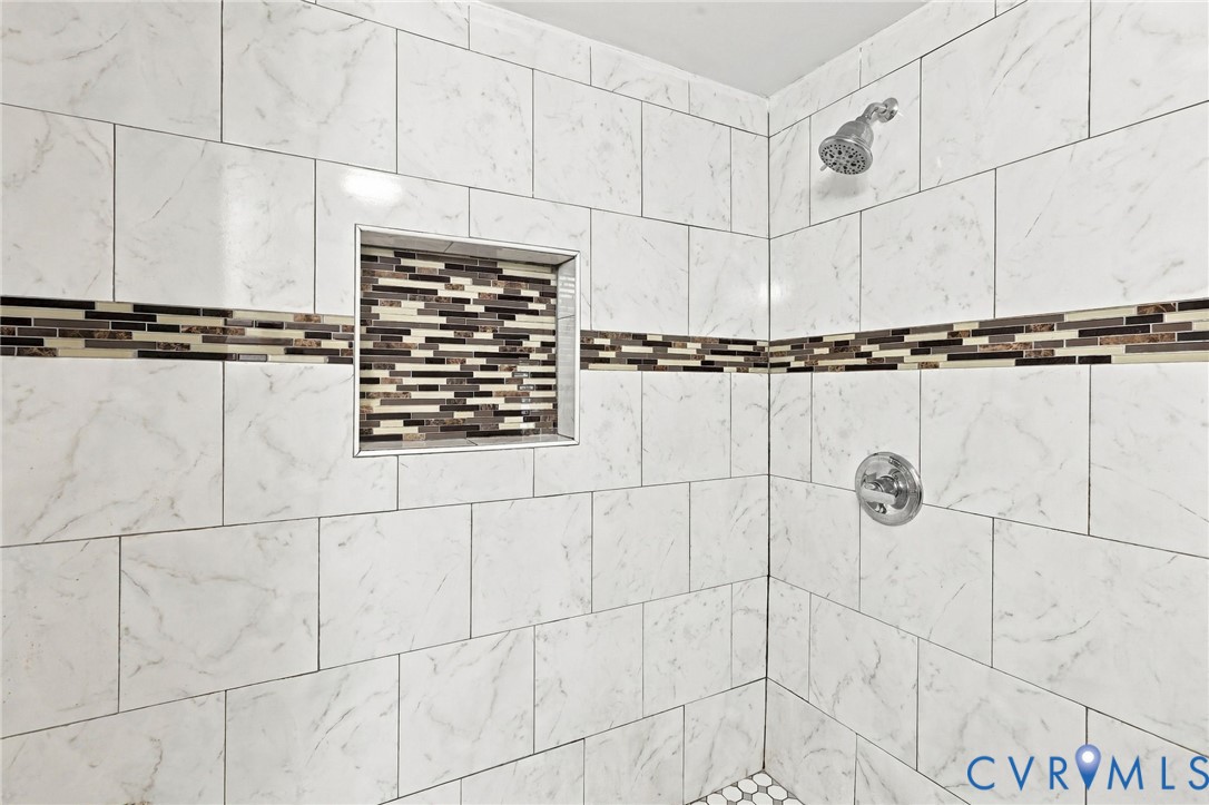 Tiled shower with white rectangular tiles, a decorative mosaic tile band, a recessed niche, and a chrome shower head and controls
