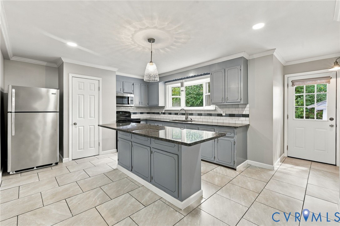 Kitchen featuring light gray cabinetry, a central island with a dark countertop, stainless steel appliances, a white subway tile backsplash, and light-toned rectangular floor tiles