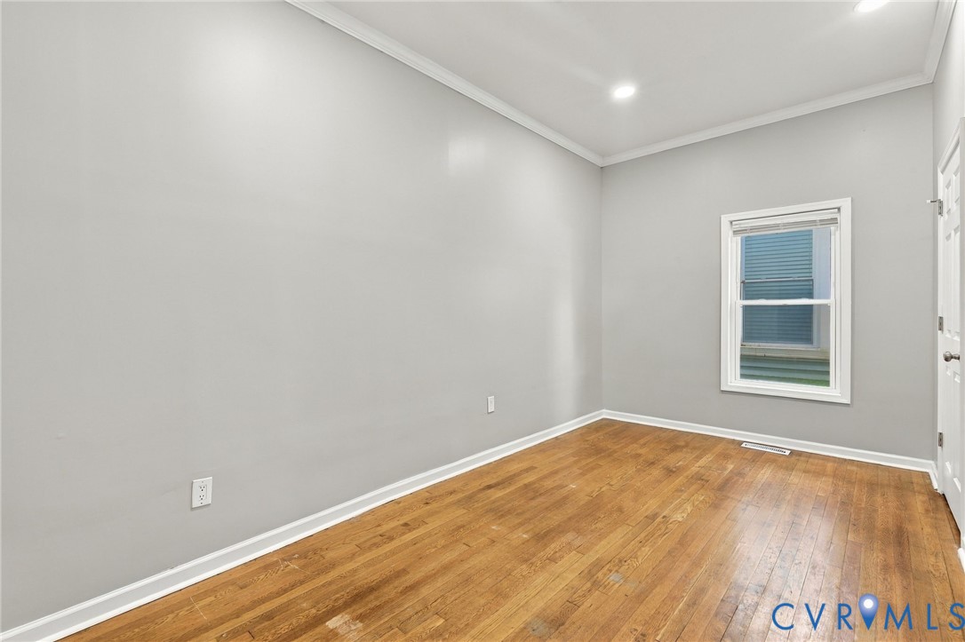 Light gray painted walls with white crown molding, recessed lighting, wood-finish flooring, and a white framed window