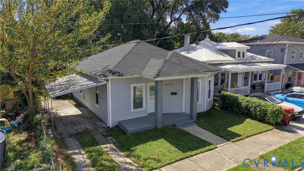 Light gray siding exterior with dark gray trim, featuring a covered front porch and a paved driveway with a carport
